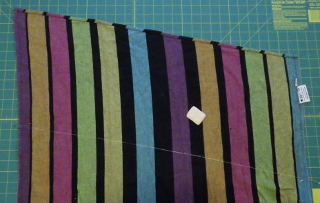 Striped woven wrap on a cutting board with tailor's chalk drawn in a line in preparation for shortening the woven wrap.
